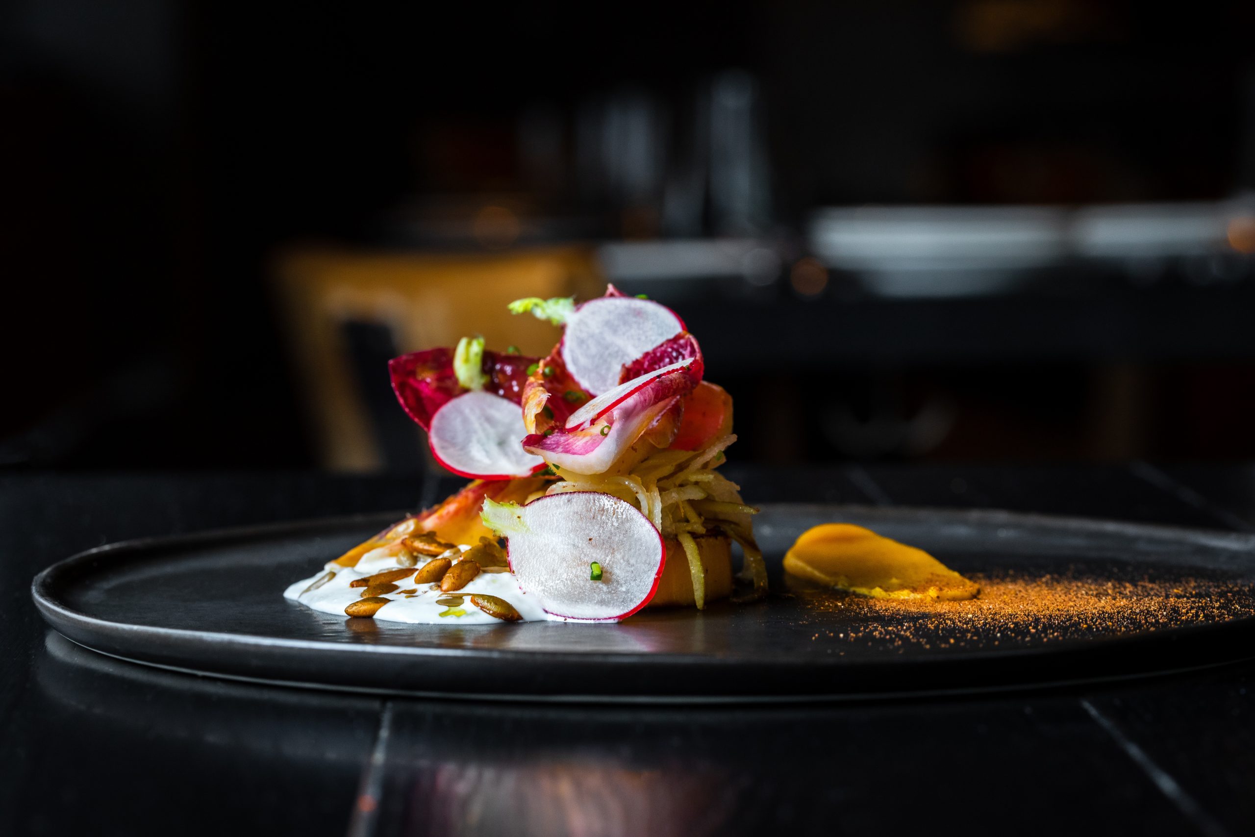 Haute cuisine salad with nuts, sauce and radish on a black dish